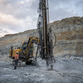 DTH drill rig operating at an open-pit hard rock bench with visible hammer and pipes