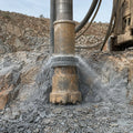 DTH drill bit penetrating hard rock surface with flushing visible at drill collar
