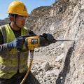 Y19A hand-held rock drill in outdoor quarry — worker drilling anchor holes into rock face, compressed air hose connected