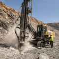 DTH hammer in active open-pit mining operation — crawler drilling rig with hammer assembly penetrating hard rock, dust and rock chips visible